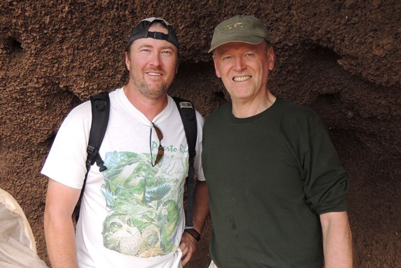 Two people standing in front of rock wall.