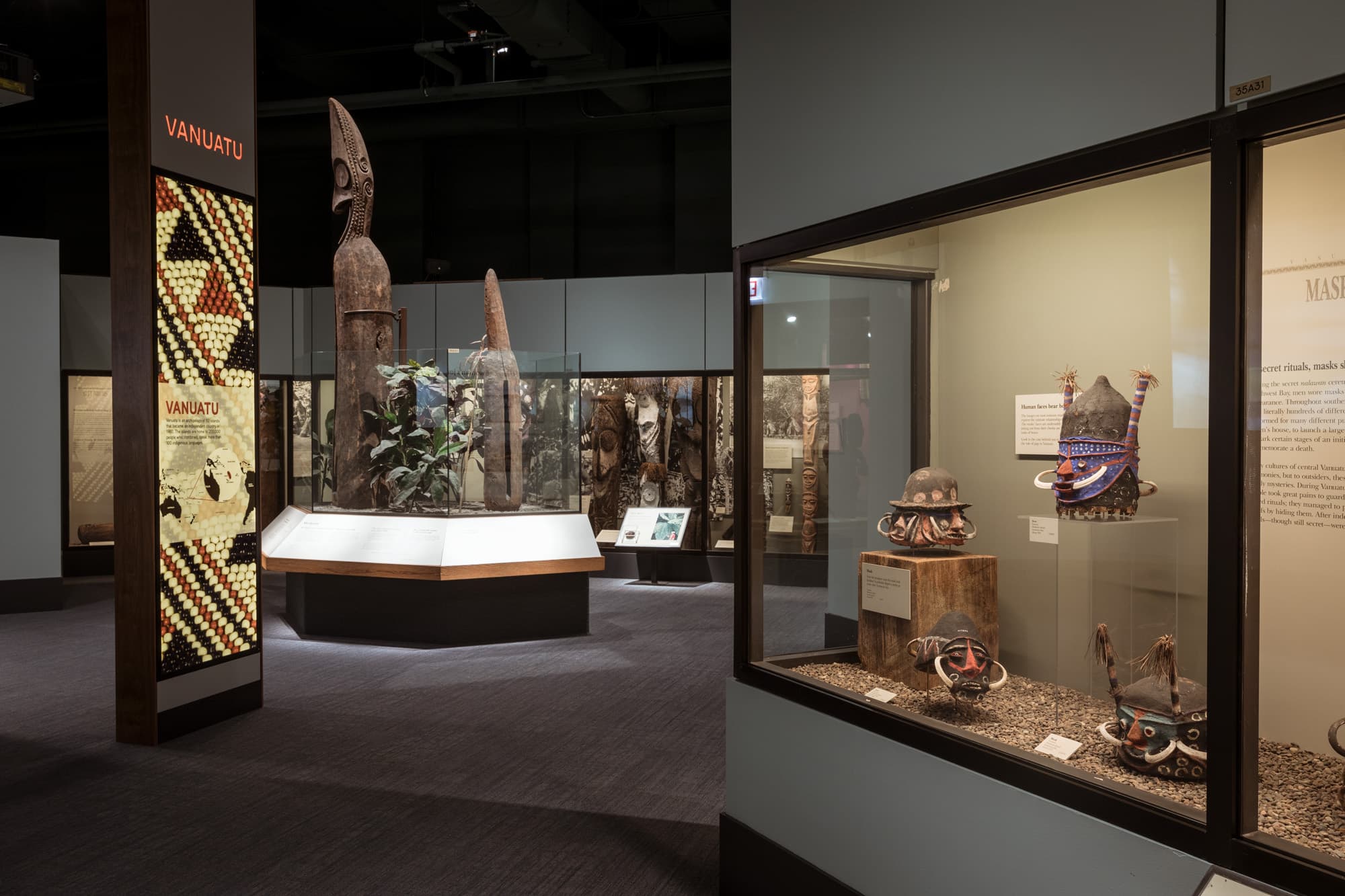 A view of cases in the Regenstein Halls of the Pacific. Various objects are arranged in cases. A large pillar with "Vanuatu" printed across the top is visible to the left.