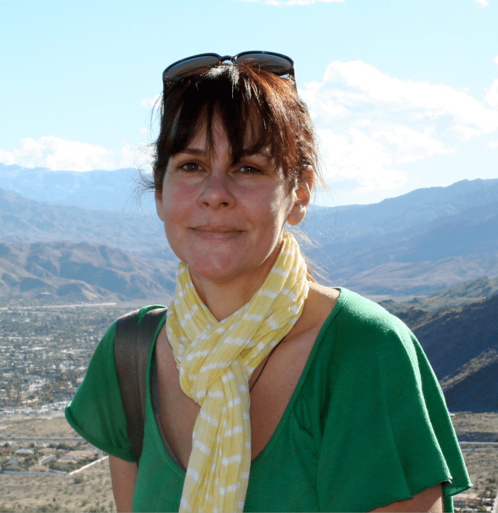 A woman wearing a green shirt and yellow scarf, low mountains on the background.