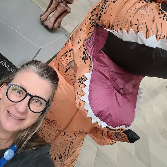 an angled image of a smiling woman next to an inflatable T. rex