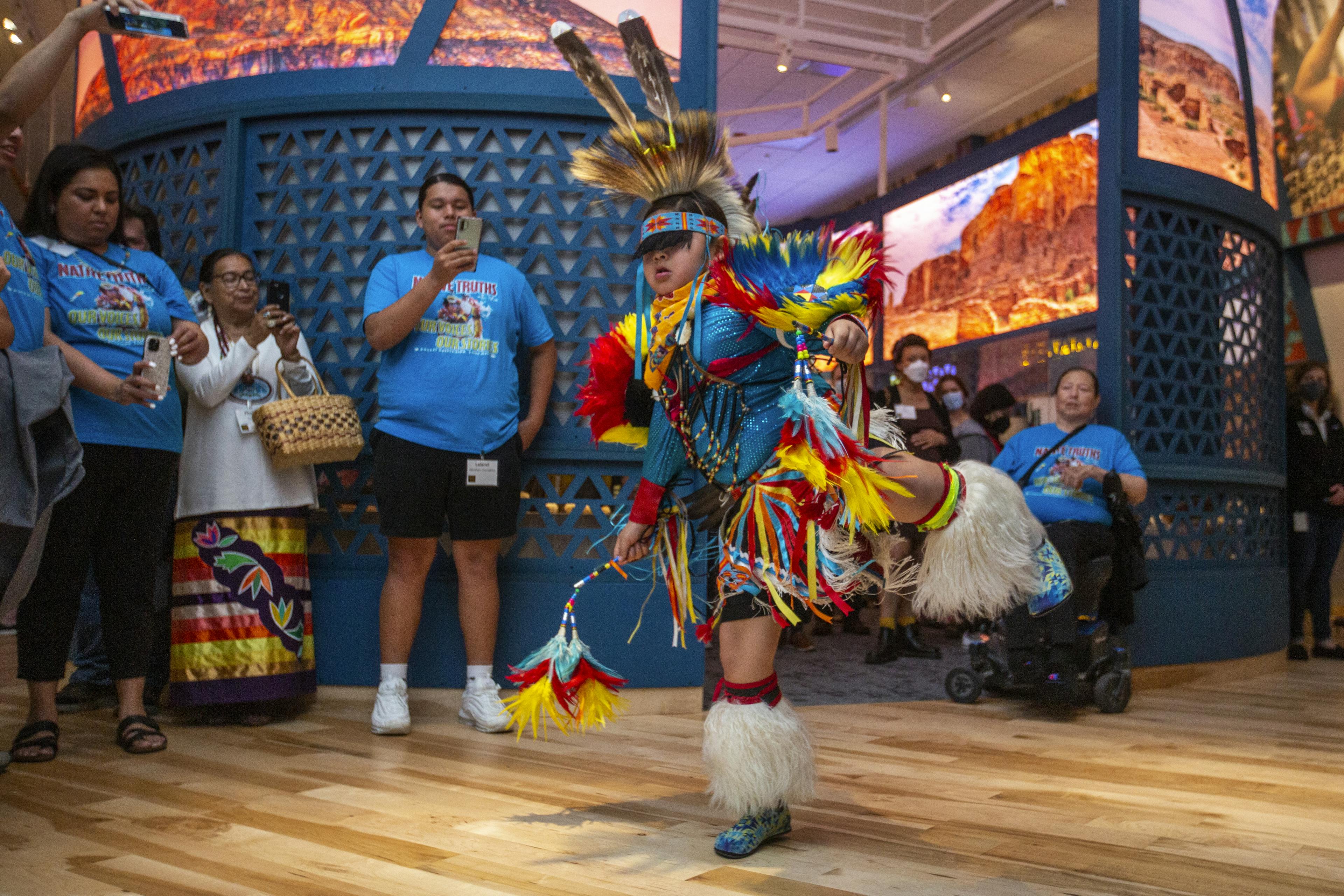 A group of visitors watch a young performer dance in the Native Truths exhibition