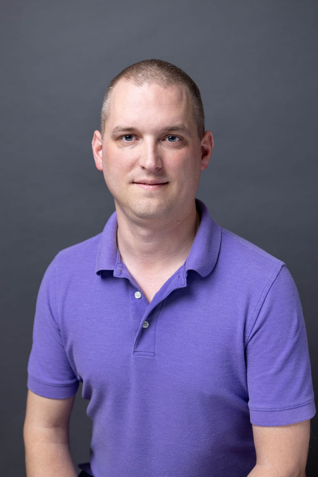 A smiling man wearing a purple shirt