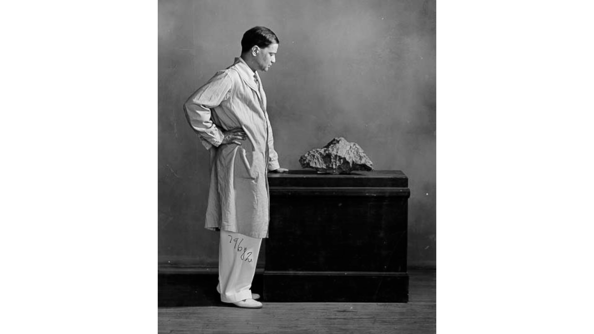 A man wearing a lab coat stands next to a display table with a large rock