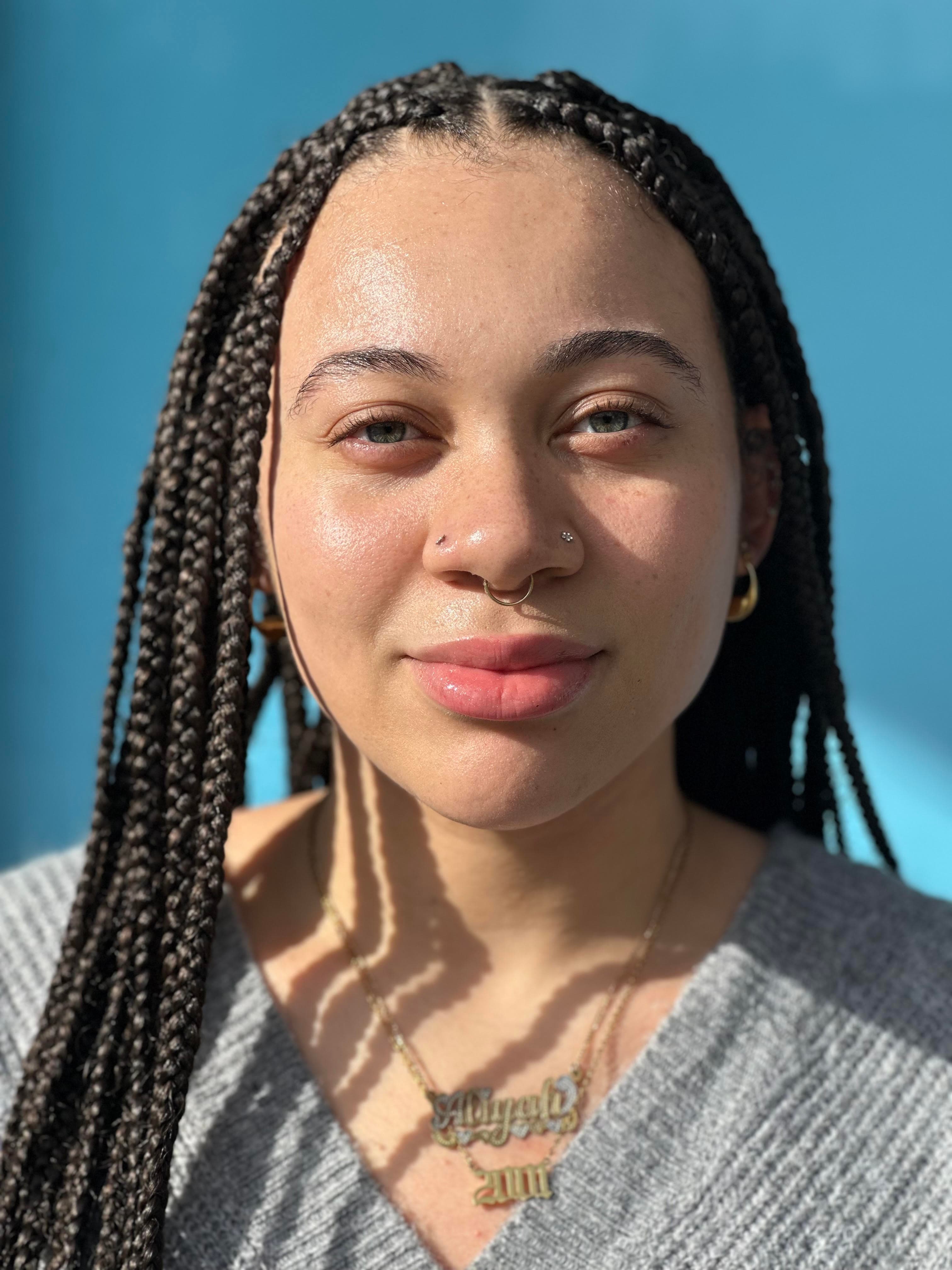 A woman with braided hair, wearing a grey sweater and gold necklace.