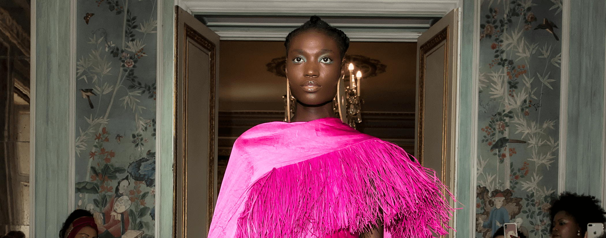 a model wearing a bright pink fringed cape